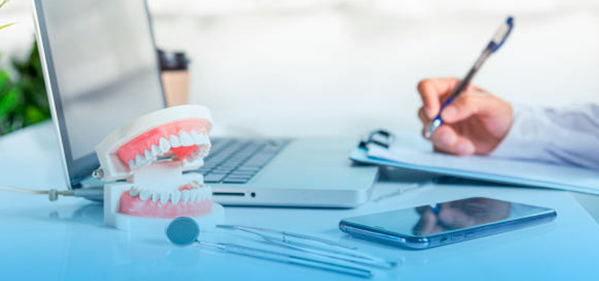 Mesa de consultório com um notebook e uma pessoa anotando como faz a emissão de NFS do Simples Dental